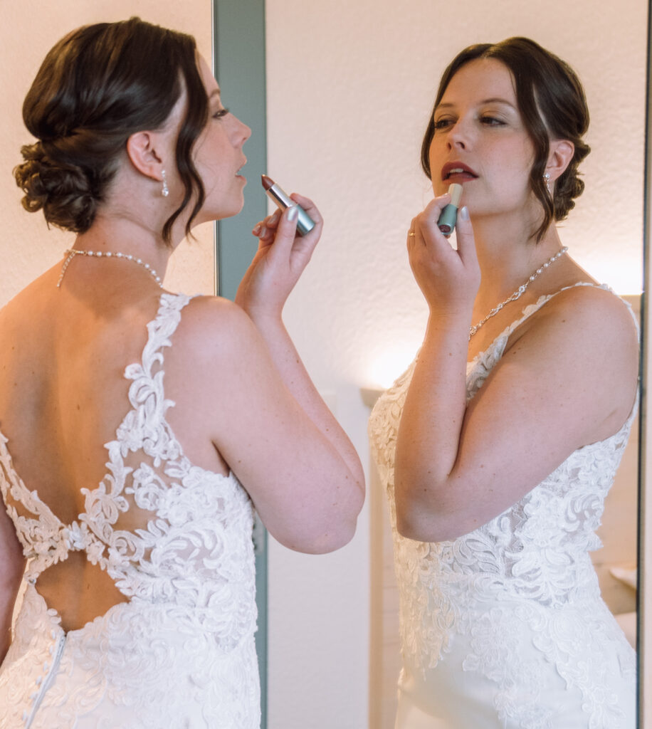„Braut trägt Spitze-Hochzeitskleid und schminkt sich vor dem Spiegel beim Getting Ready vor der Hochzeit in Ingolstadt.“