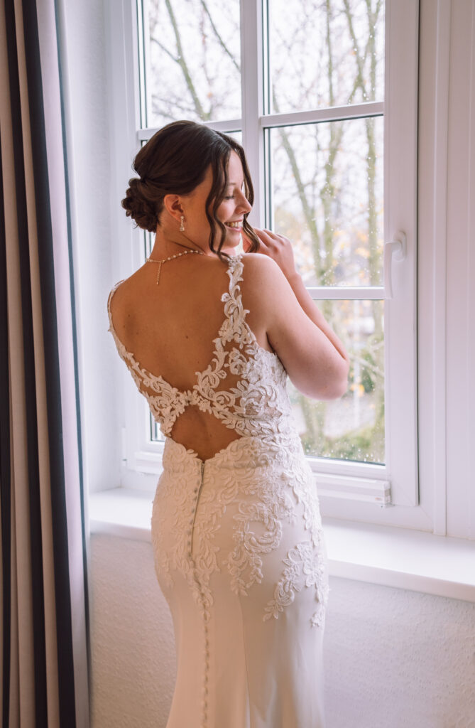 „Elegantes Bridal Getting Ready Portrait am Fenster mit Spitze und Rückenansicht des Brautkleids.“