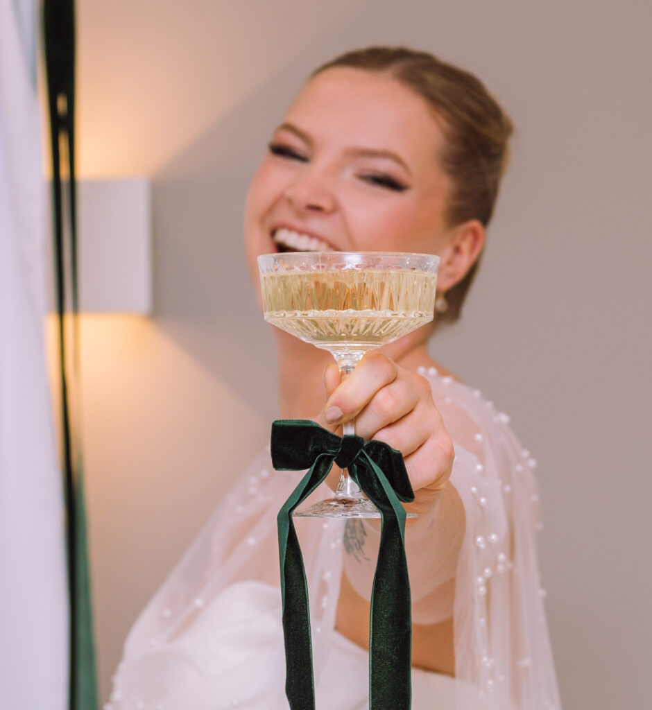 „Braut stößt mit Champagner bei der Hochzeit in Ingolstadt an und lächelt in die Kamera.“