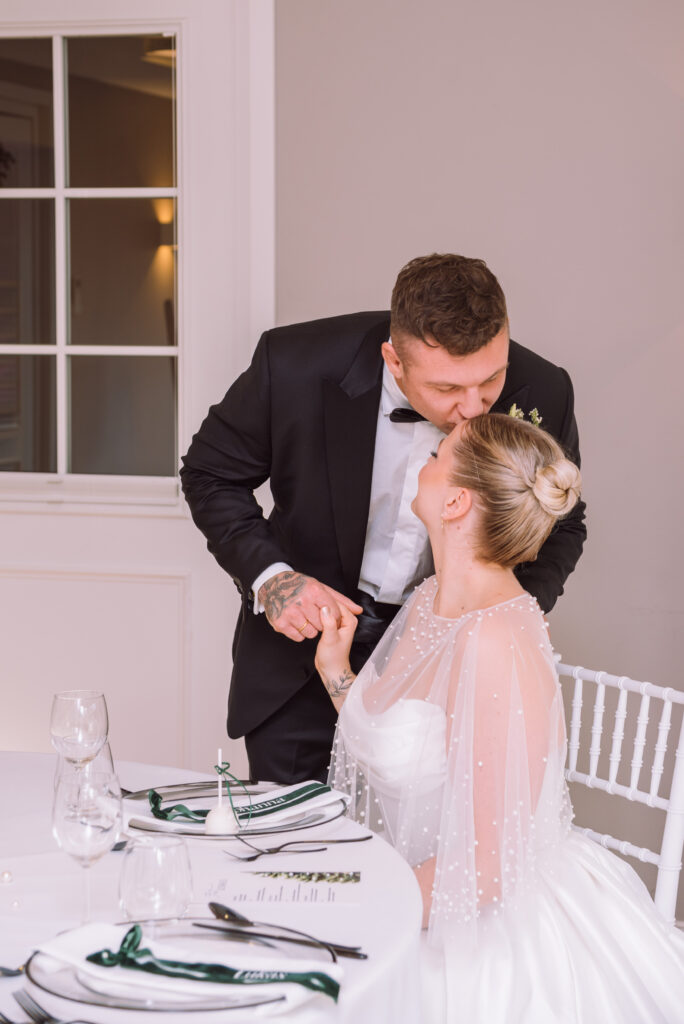 „Bräutigam küsst seine Braut während des Hochzeitsdinners bei einer Hochzeit in Ingolstadt.“