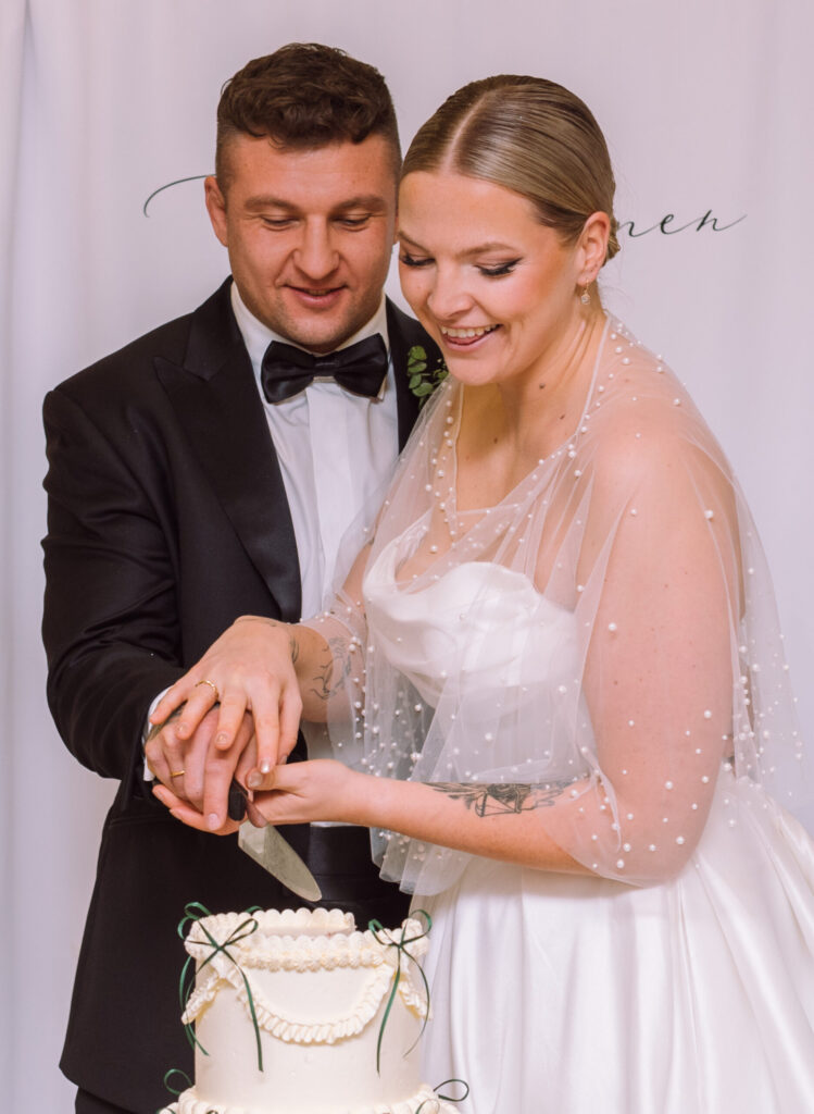 „Braut und Bräutigam schneiden gemeinsam die Hochzeitstorte bei ihrer Hochzeit in Eichstätt auf Schloss Hirschberg an.“