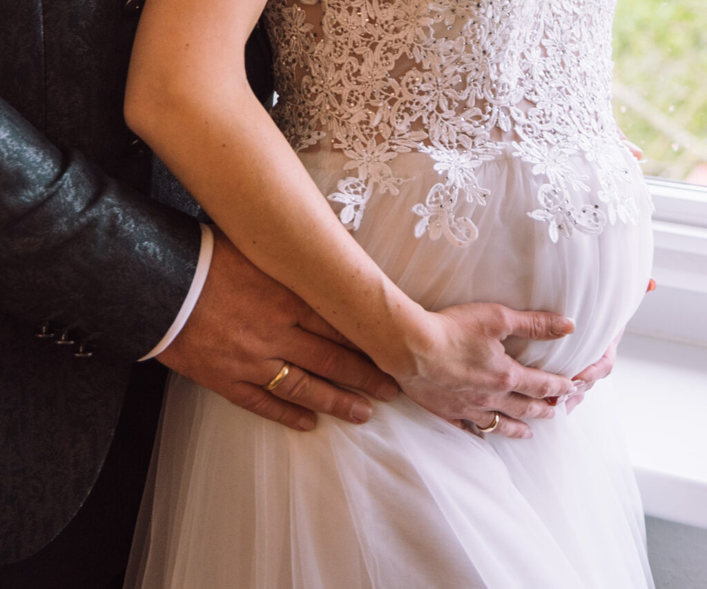 „Detailaufnahme eines Brautpaars bei einer Hochzeit in Ingolstadt – Hände mit Eheringen und Brautkleid.“